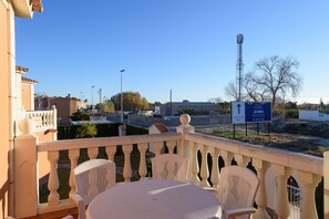 Uma varanda com cadeiras e mesa brancas, com vista para um céu limpo e uma placa com 'Las Dunas'.