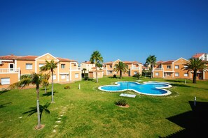 Resort com vários edifícios de dois andares, uma piscina central e palmeiras.