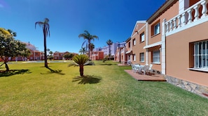 A courtyard with a lawn, palm trees, and a building with balconies and windows. - Amaranto by ON Travel (Oliva)