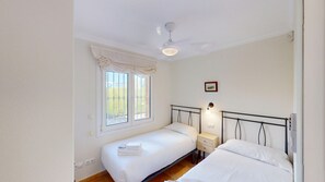 Une chambre avec deux lits, une fenêtre donnant sur un beau paysage, un ventilateur de plafond et une table de chevet avec une lampe.