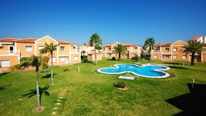 Ein Resort mit mehreren zweigeschossigen Gebäuden, einem zentral gelegenen Pool und Palmen.