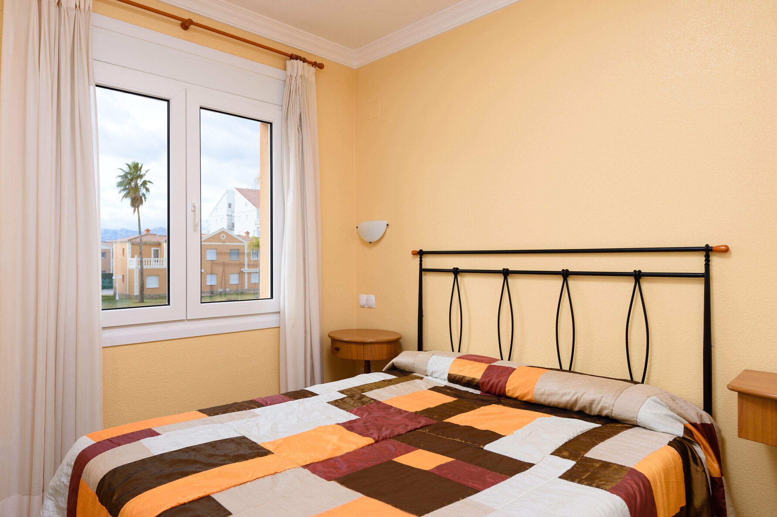 A bedroom with a bed, a window, a bedside table, and a view of buildings outside.