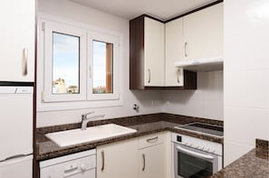 Een moderne keuken met witte kasten, een granieten aanrechtblad, een inbouwoven en een raam met uitzicht.