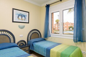 A room with two beds, a window with curtains, a wall-mounted light, and a framed picture. - Gazania by ON Travel (Oliva)