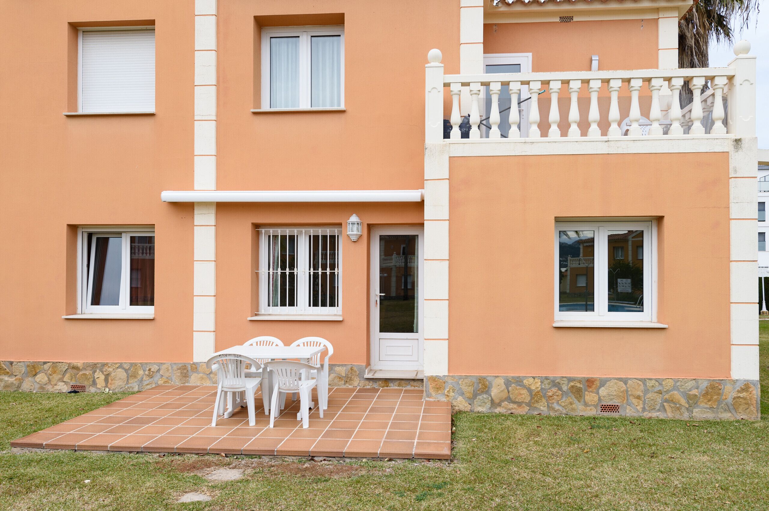 Un edificio de dos pisos con patio empedrado, ventanas de marco blanco y base de piedra.
