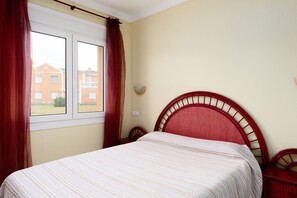 Un dormitorio con cama, ventana con cortinas y vistas a edificios.