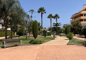 A paved walkway with benches, palm trees, and a building with solar panels. - Penthouse in Denia (Denia)