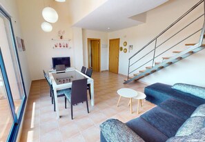 A modern living room with a sofa, a dining table with chairs, a staircase, and a door. - Penthouse in Denia (Denia)