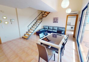 Un vaste espace de vie comprenant un escalier, une table à manger avec des chaises, un canapé et une cuisine visible à travers une porte ouverte.