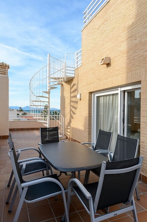 A terrace with a table and chairs, a spiral staircase, and a view of the sea. - Denia Beachfront apartment by ON Travel (Denia)