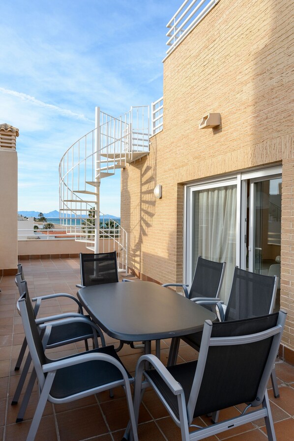 A terrace with a table and chairs, a spiral staircase, and a view of the sea.