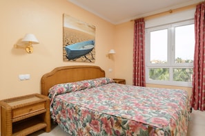 A bedroom with a bed, two nightstands, a wall-mounted lamp, a painting, and a window with curtains. - Denia Beachfront apartment by ON Travel (Denia)