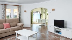 A living room with a sofa, coffee table, TV, and dining area with chairs and a table. - Villa Mar by ON Travel (Oliva)