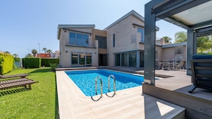 Et moderne hus med swimmingpool, terrasse med havemøbler og en velplejet græsplæne.