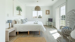 A bedroom with a bed, a television, a wicker chair, and a large window. - Villa Panorama  (Oliva)