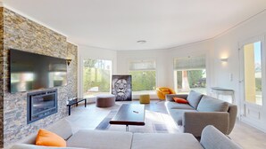 Una sala moderna con pared de piedra, televisor de pantalla plana, chimenea y un ventanal con vistas al exterior.