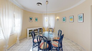 A dining area with a round glass table, six chairs, and a white cabinet. - Villa Golden by ON Travel (Oliva)