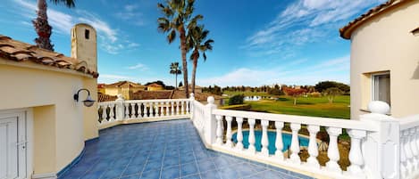A balcony with a pool, palm trees, and a golf course view.