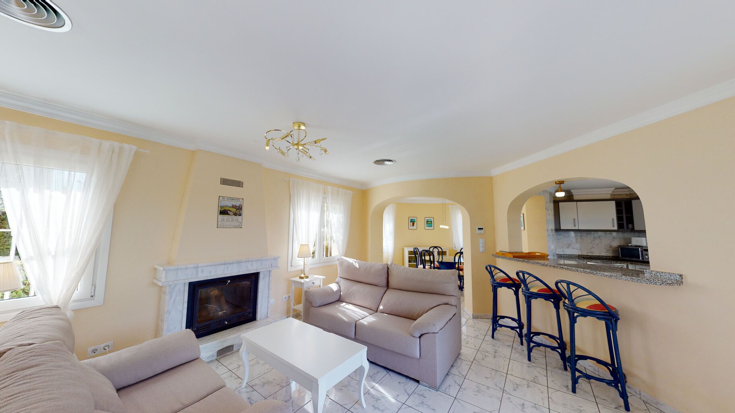 A living room with a sofa, TV, and fireplace, leading to a kitchen with bar stools.