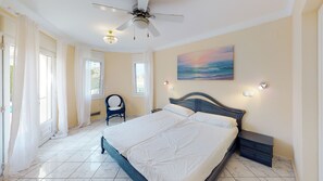 A bedroom with a bed, a ceiling fan, a chair, and a painting on the wall. - Villa Golden by ON Travel (Oliva)