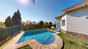 Una piscina con bordo piastrellato, un muro in pietra e un edificio con tetto in tegole.