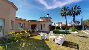 Propiedad residencial con patio, mobiliario exterior, piscina y palmeras.