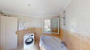 Un baño con lavadora, bañera y ventana con vistas.