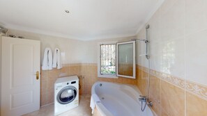 A bathroom with a washing machine, a bathtub, and a window with a view.