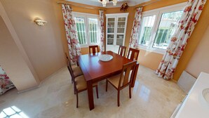 Un comedor con una mesa y sillas de madera, un armario con puertas de vidrio y cortinas con motivos florales.