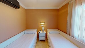 A hotel room with two single beds, a bedside table with a lamp, and a wall-mounted air conditioning unit. - Villa Boreal by ON Travel (Oliva)