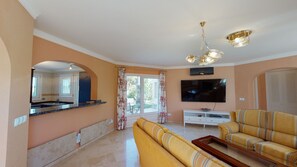 Una sala de estar con un sofá, un televisor y un comedor con ventana.