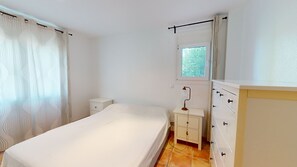 Ein Schlafzimmer mit Bett, Nachttisch, Kommode, Fenster und Vorhängen.