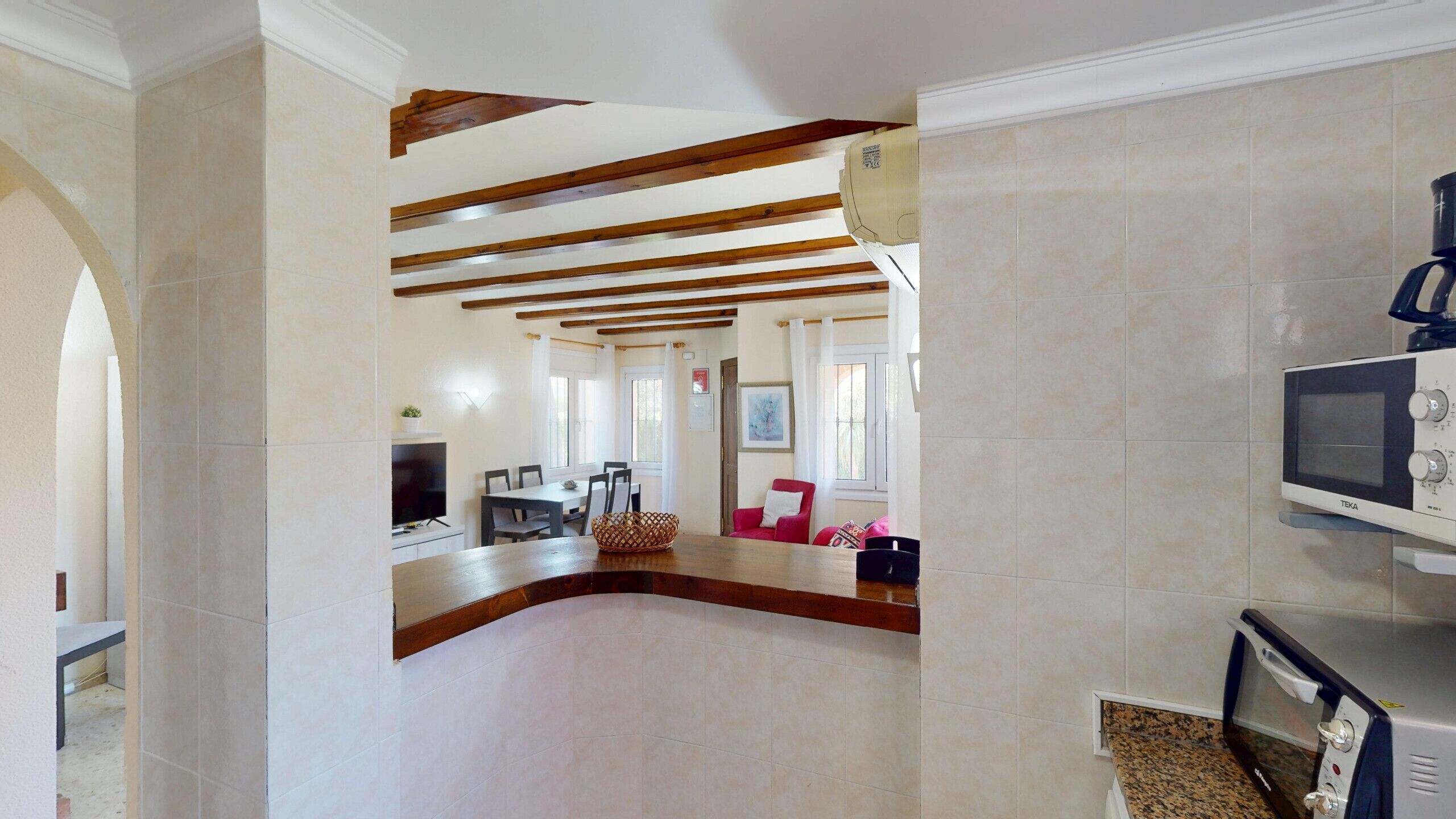 A spacious living area with a high ceiling, exposed wooden beams, a television, and a microwave.