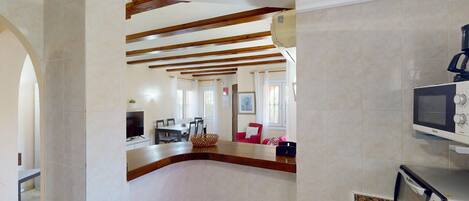 A spacious living area with a high ceiling, exposed wooden beams, a television, and a microwave.