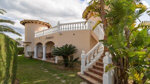 Un edificio de dos plantas con fachada color beige, columnas blancas y una escalera con barandilla blanca.