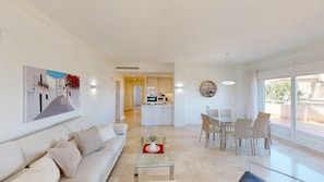 A modern living room with a sofa, a glass coffee table, and a dining area with chairs and a table.