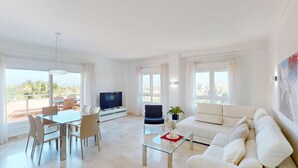 A modern living room with a dining area, a sofa, a TV, and a balcony with a view.