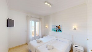 A hotel room with two beds, a TV, a painting, and a balcony with a view.