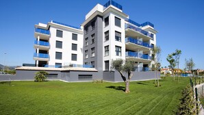 A modern multi-story building with balconies, a well-maintained lawn, and a clear blue sky.