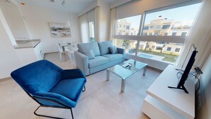 Een moderne woonkamer met een blauwe fauteuil, een grijze bank, een glazen salontafel en een tv op een dressoir.