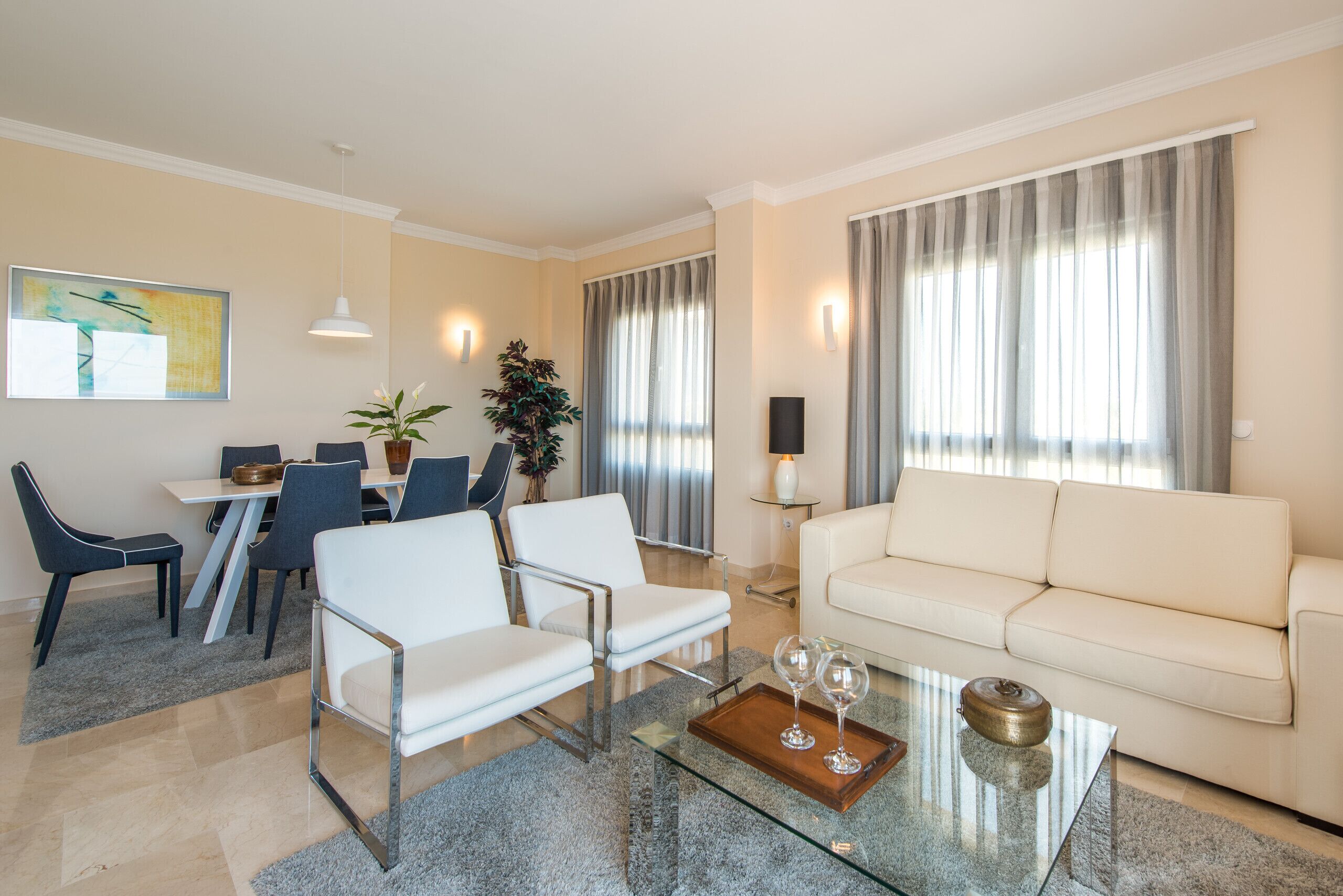 Un salon moderne avec une table basse en verre, un canapé blanc et des fauteuils bleus.