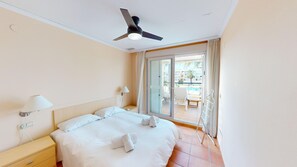 Une chambre d’hôtel avec un lit, des lampes de chevet, un ventilateur de plafond et une vue sur l’espace extérieur de la piscine.