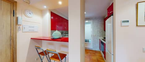Una cocina con armarios rojos, un refrigerador blanco, un lavamanos y un reloj en la pared.