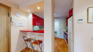 Une cuisine avec des meubles de rangement rouges, un réfrigérateur blanc, un évier et une horloge au mur.
