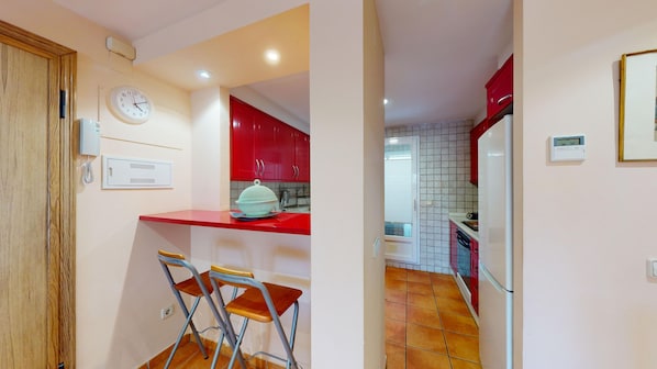 Una cocina con armarios rojos, un refrigerador blanco, un lavamanos y un reloj en la pared.