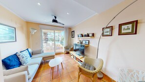 Sala de estar com sofá, televisão, poltrona de vime e varanda com vista.