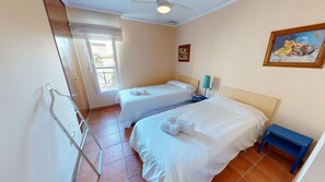A hotel room with two beds, a window with blinds, a painting on the wall, and a blue nightstand. - Arena y Brisa by ON Travel (Oliva)