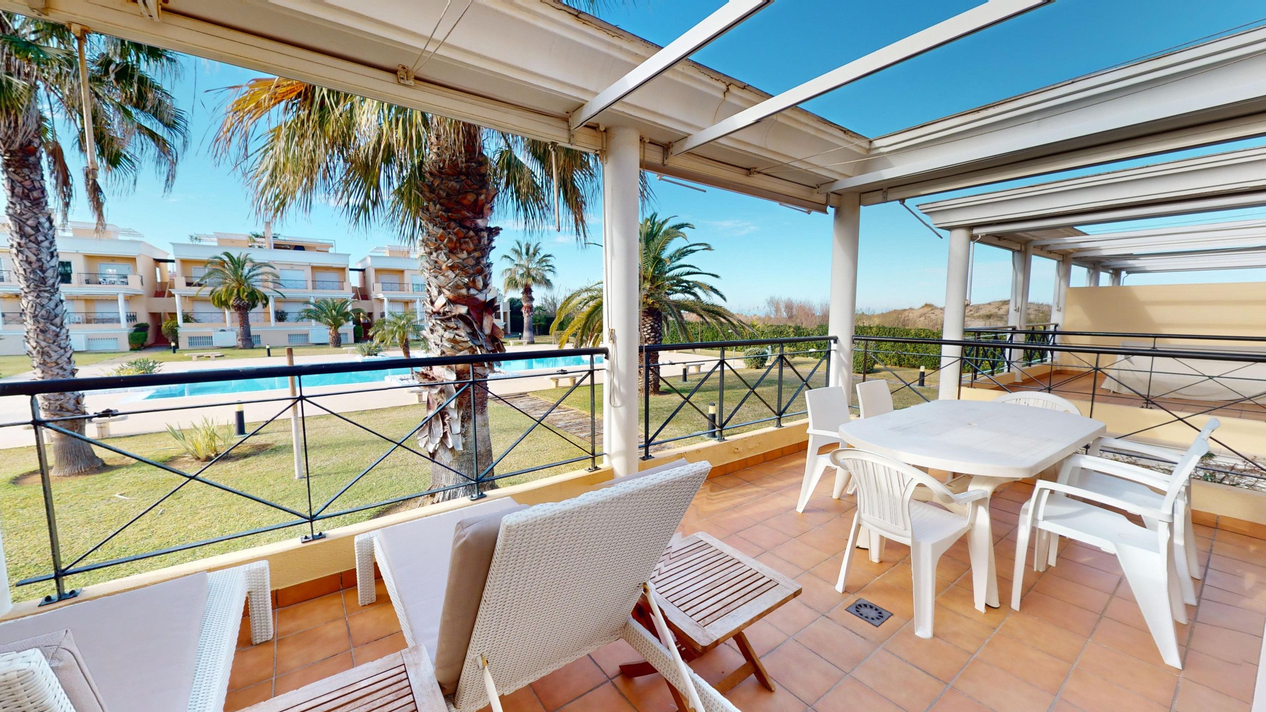 A covered outdoor area with a pool, palm trees, and a view of a building complex.