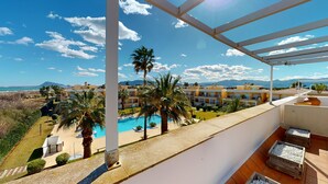 Un balcón con vistas a una piscina, palmeras y una cordillera.