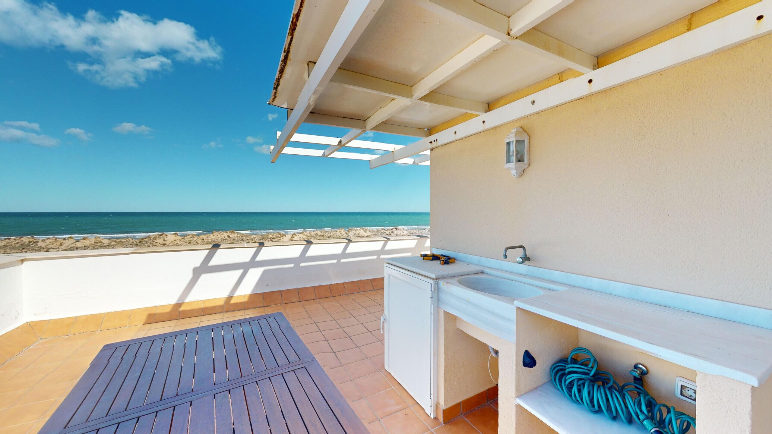 Ein Balkon mit Blick auf den Strand, ein kleines Waschbecken und ein aufgerollter Gartenschlauch.